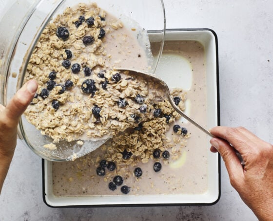Person pouring mixture for blueberry lemon baked oatmeal into a baking dish.