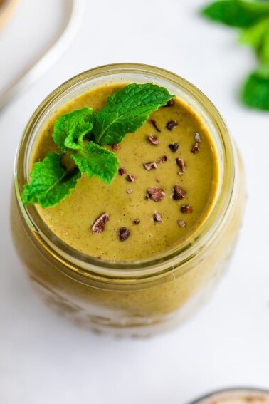 Mason jar with a mint chocolate chip smoothie garnished with cacao nibs and mint.