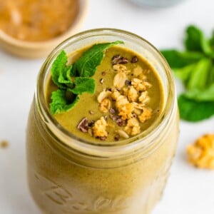 Mason jar with a mint chocolate chip smoothie garnished with cacao nibs, granola and mint.
