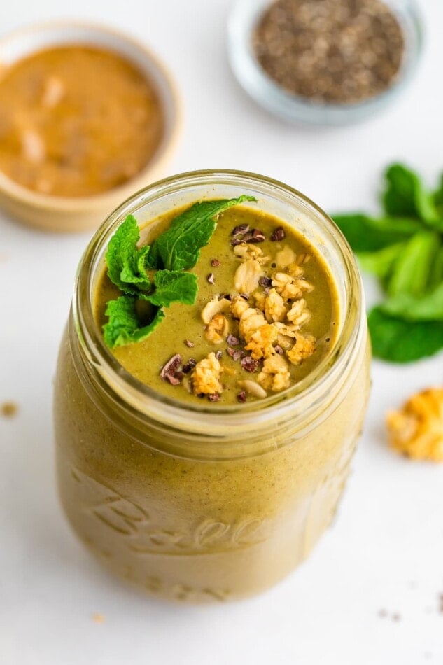 Mason jar with a mint chocolate chip smoothie garnished with cacao nibs, granola and mint.