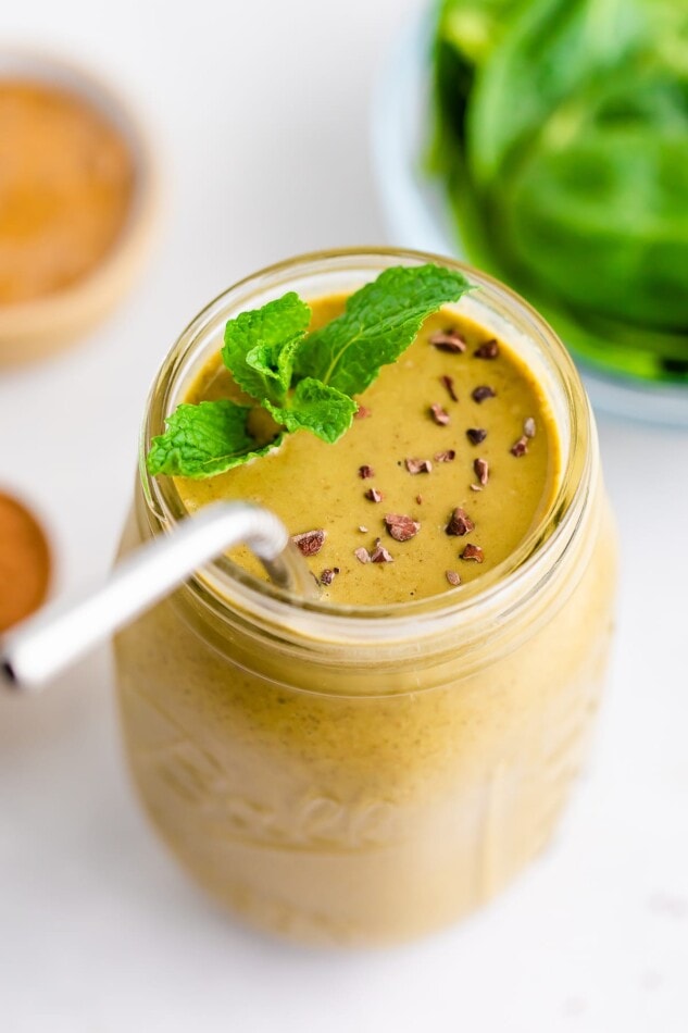 Mason jar with a mint chocolate chip smoothie garnished with cacao nibs and mint.