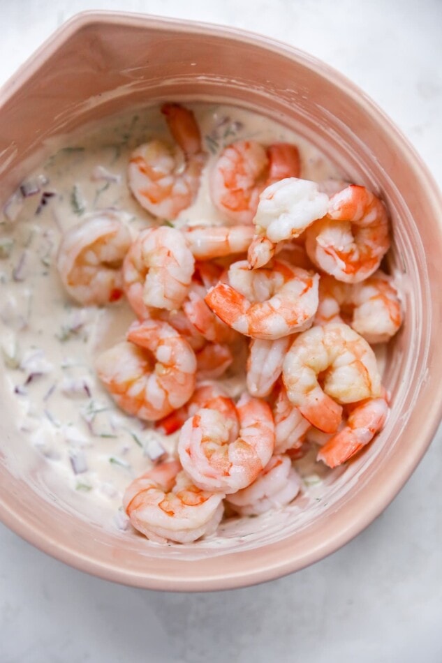 Mixing bowl with creamy dressing and cooked shrimp.