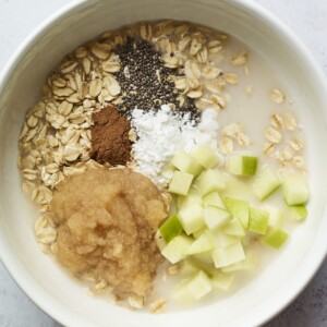 Oats, cinnamon, chia seeds, baking powder, apple chunks and applesauce in a mixing bowl.