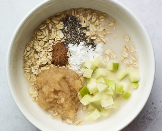 Oats, cinnamon, chia seeds, baking powder, apple chunks and applesauce in a mixing bowl.