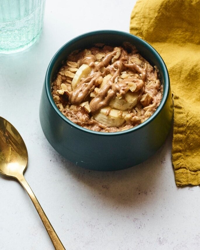 Bowl of banana walnut baked oatmeal. A spoon, napkin and glass of water are next to the bowl.