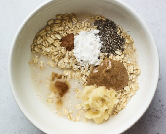 Oats, cinnamon, baking powder, almond butter, chia seeds, almond milk and banana in a bowl.