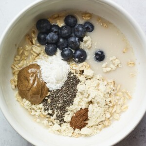Bowl with blueberries, protein powder, cinnamon, almond milk, chia seeds, oats and almond butter.