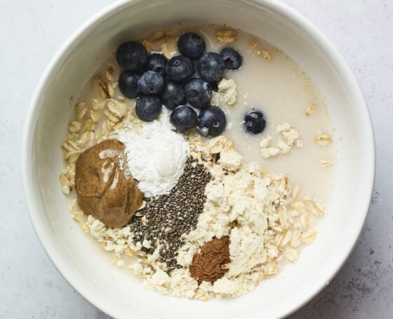 Bowl with blueberries, protein powder, cinnamon, almond milk, chia seeds, oats and almond butter.