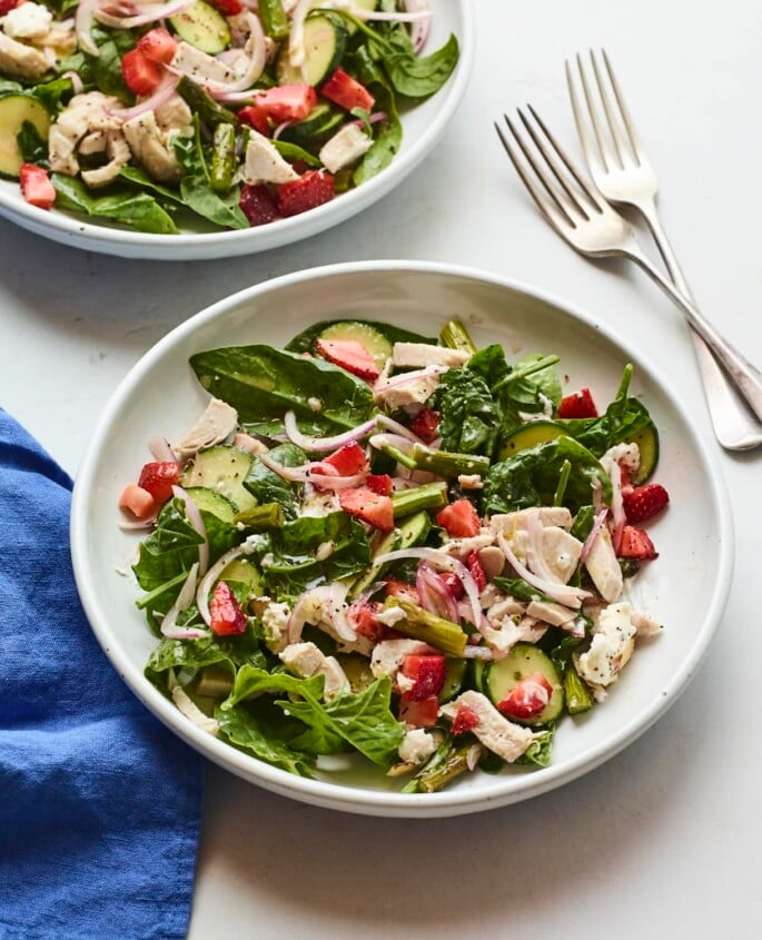 White plate with a chopped spinach salad with strawberries and chicken.