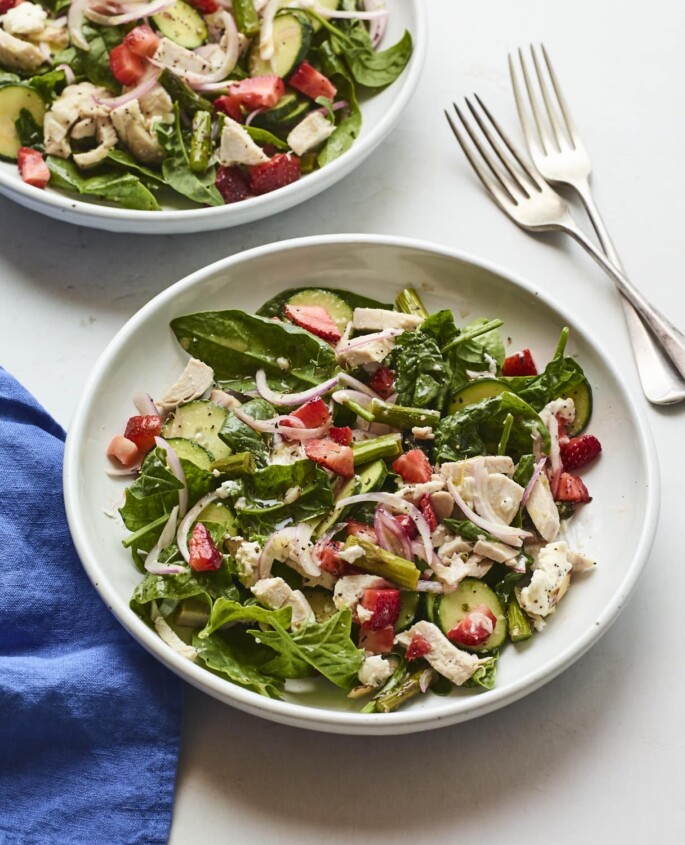 White plate with a chopped spinach salad with strawberries and chicken.