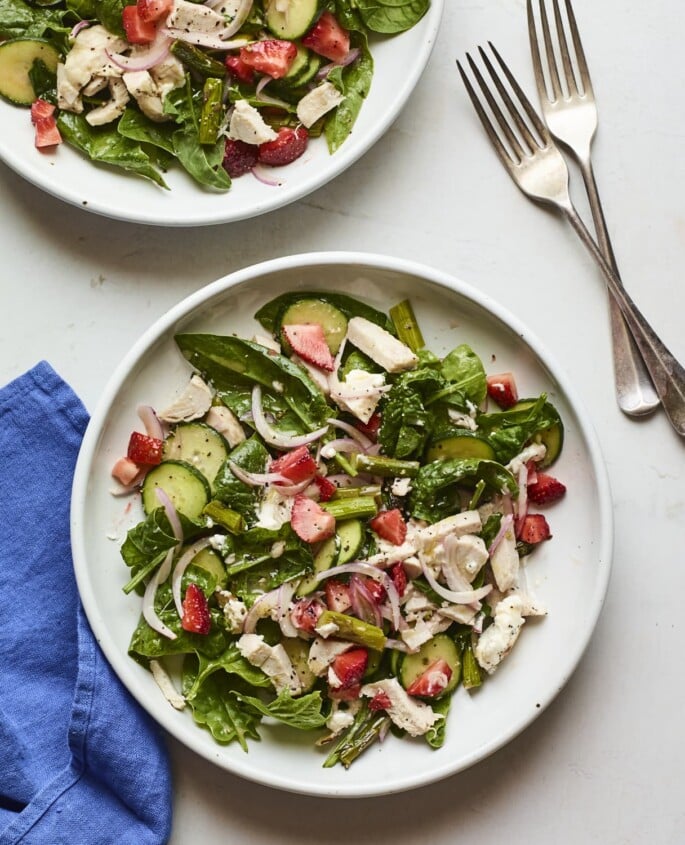 White plate with a chopped spinach salad with strawberries and chicken.