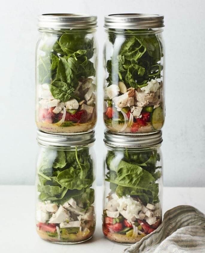 Four mason jars filled with a strawberry spinach chicken salad.