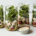 Four mason jars filled with a strawberry spinach chicken salad.