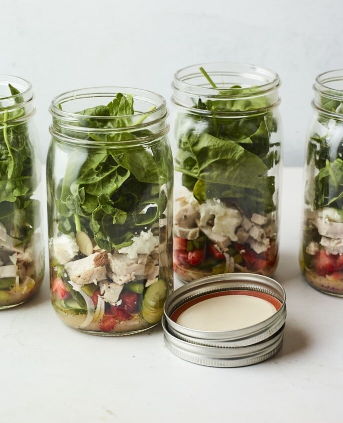 Four mason jars filled with a strawberry spinach chicken salad.