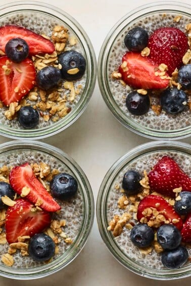 Four glass jars with chia pudding topped with fruit and granola.