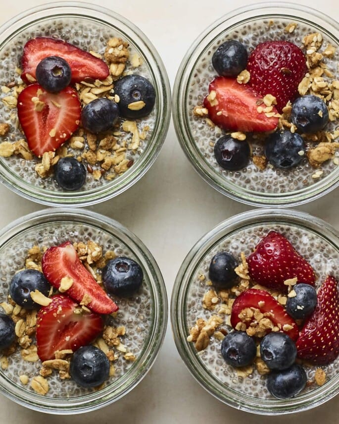 Four glass jars with chia pudding topped with fruit and granola.