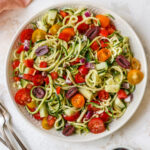 Serving bowl of zucchini noodle salad with tomatoes, peppers and olives.