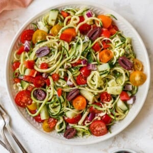 Serving bowl of zucchini noodle salad with tomatoes, peppers and olives.