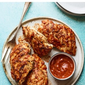 Plate with 4 bbq chicken breasts and a bowl of homemade bbq sauce.