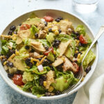 Bowl with bbq chicken salad. A fork is in the bowl and a napkin and glass of water are beside the bowl.