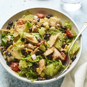 Bowl with bbq chicken salad. A fork is in the bowl and a napkin and glass of water are beside the bowl.