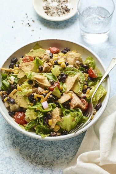 Bowl with bbq chicken salad. A fork is in the bowl and a napkin and glass of water are beside the bowl.