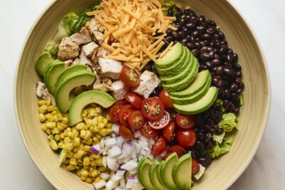 Salad bowl with corn, onion, avocado, tomato, bbq chicken, cheese, lettuce and black beans.
