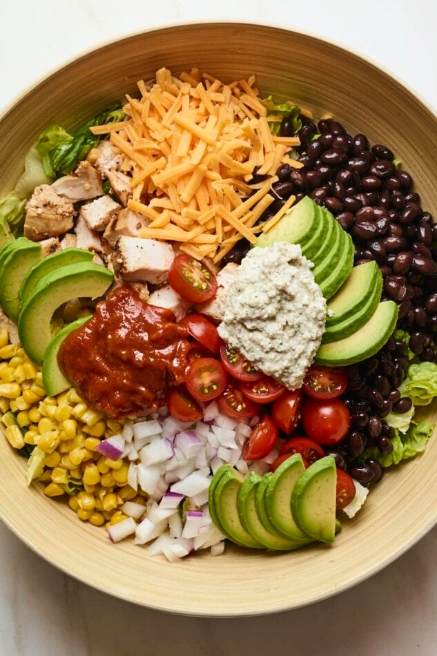 Salad bowl with corn, onion, avocado, tomato, bbq chicken, cheese, lettuce, ranch and black beans.