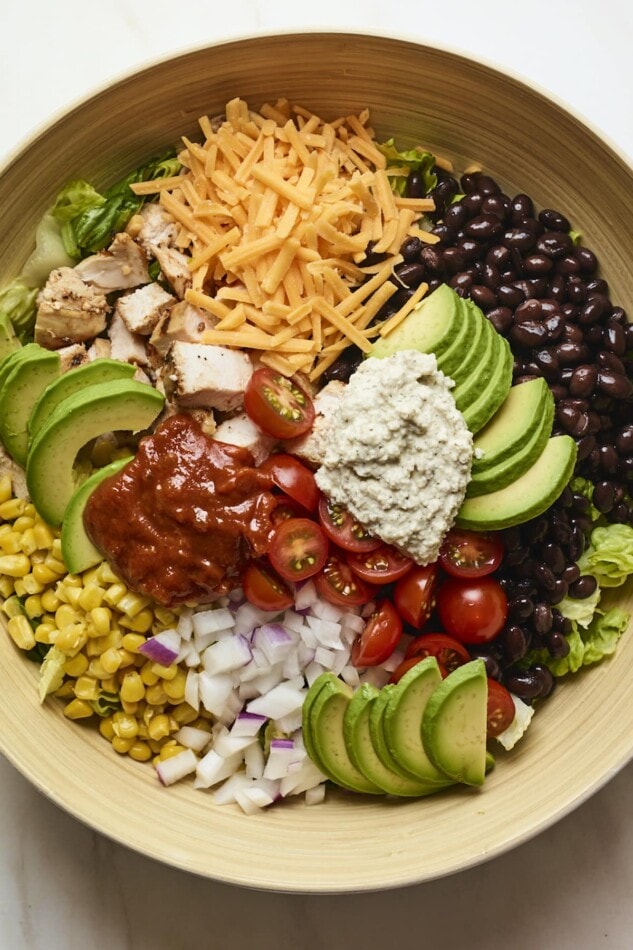 Salad bowl with corn, onion, avocado, tomato, bbq chicken, cheese, lettuce, ranch and black beans.