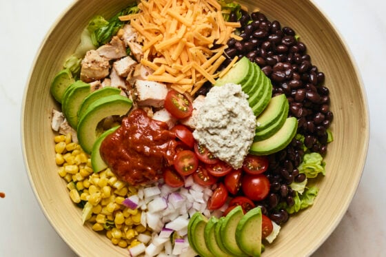 Salad bowl with corn, onion, avocado, tomato, bbq chicken, cheese, lettuce, ranch and black beans.