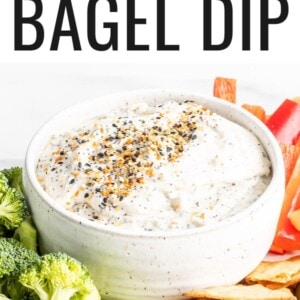 Everything bagel dip in a bowl. Veggies and pita chips are around the bowl of dip.