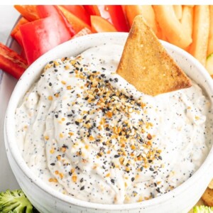 Everything bagel dip in a bowl. Veggies and pita chips are around the bowl of dip.