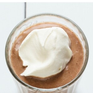 Chocolate protein shake in a glass topped with whipped cream.