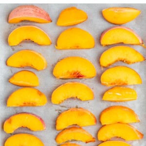 Frozen peach slices on a parchment paper lined cookie sheet.