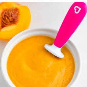 Bowl of peach baby food with a baby spoon.
