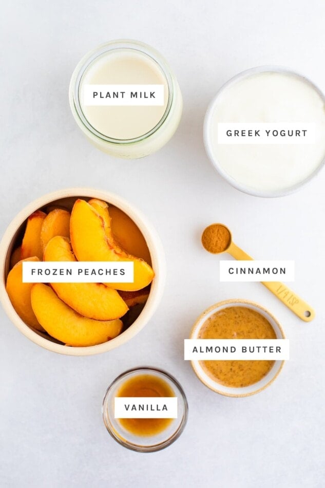 Ingredients measured out to make peach smoothies: plant milk, greek yogurt, frozen peaches, cinnamon, almond butter and vanilla.