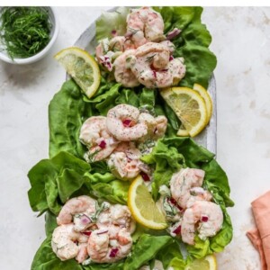 Serving platter with shrimp salad served in lettuce cups. Lemon wedges are garnishing the plate.