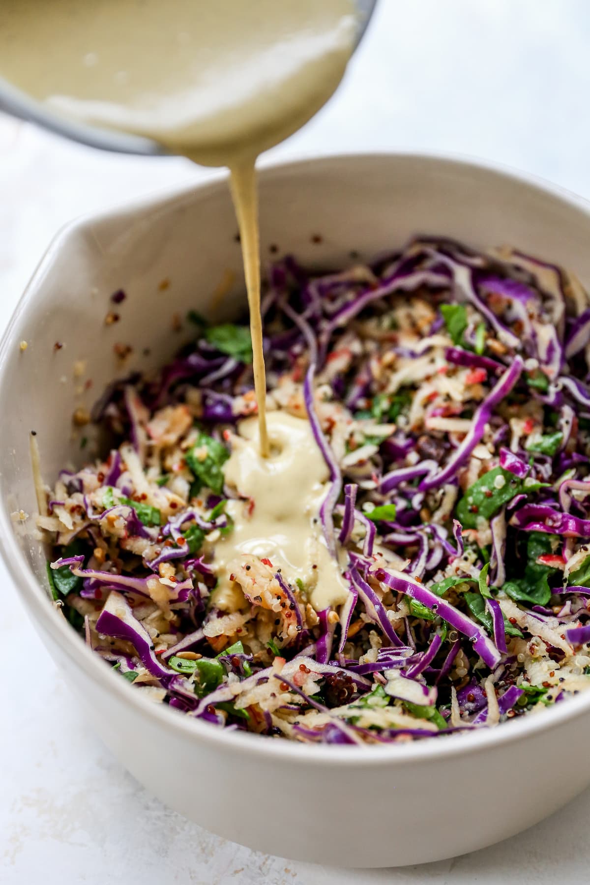 Pouring tahini dressing over cabbage apple slaw.