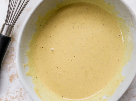 Tahini dressing in a bowl next to a whisk.