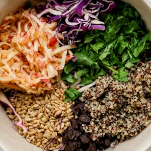 Shredded apples, cabbage, spinach, quinoa, raisins and sunflower seeds in a bowl.