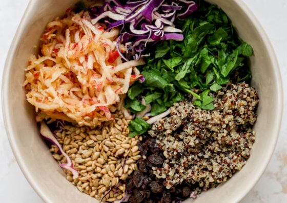 Shredded apples, cabbage, spinach, quinoa, raisins and sunflower seeds in a bowl.