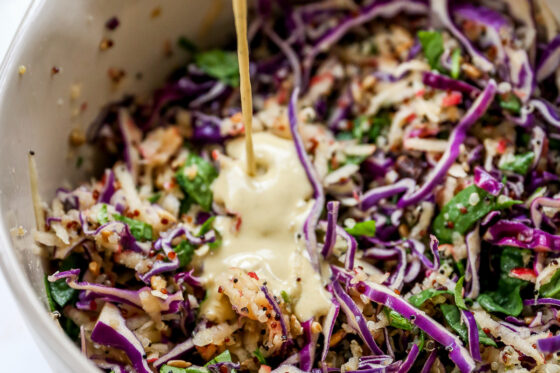 Tahini dressing being poured over a bowl of apple slaw.