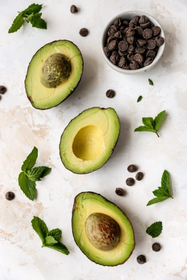 Avocados, mint leaves and chocolate chips on a table top.