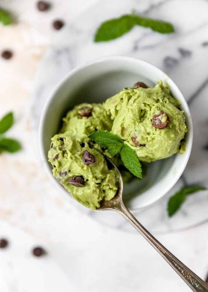 Bowl of avocado mint chocolate chip ice cream garnished with fresh mint. Spoon is taking a bite.