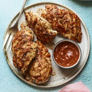 Plate with 4 bbq chicken breasts and a bowl of homemade bbq sauce.