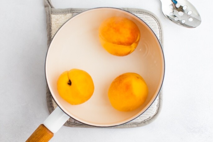 Three peaches in a white pot with water.