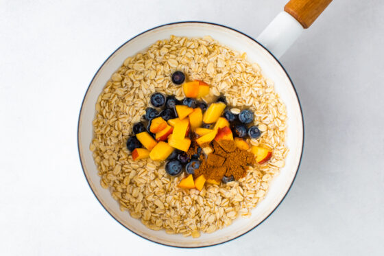 White saucepan with oatmeal, water, blueberries, chopped peaches and cinnamon.