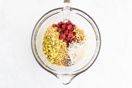 Cereal, dried cranberries, seeds and coconut in a glass mixing bowl.