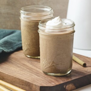 Chocolate protein shake in in two mason jars topped with whipped cream.