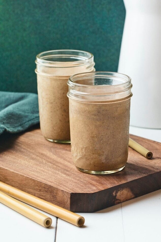Two mason jars with coffee protein shakes on a wooden board with wooden straws.